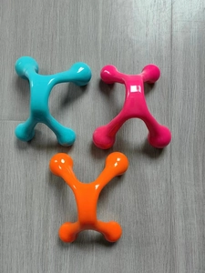 Three handheld four-point manual massagers in blue, pink, and orange on wood surface