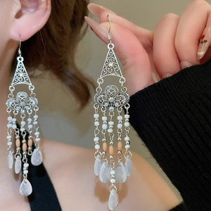 Close-up of Bohemian triangle earrings with white beads and long tassels on model