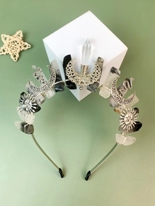 Detailed view of silver crystal headband with moon and sun charms on a geometric stand