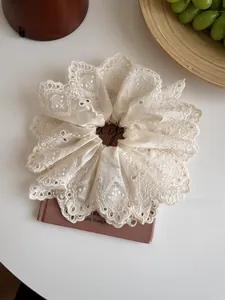Detailed view of beige lace embroidered scrunchie placed on vintage books