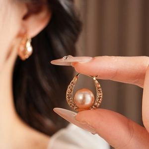 Close-up of vintage gold U-shaped earring featuring pavé crystals and a champagne pearl