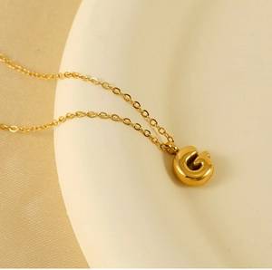 Macro detail of golden 3D bubble letter G pendant on fine chain necklace with shiny finish