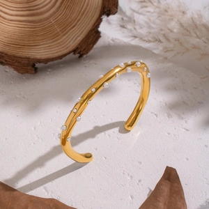 Gold plated stainless steel open bangle with white pearls on a natural textured background