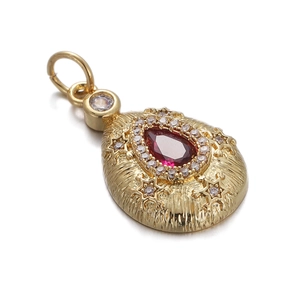 Detail of a gold pendant with a red teardrop gemstone and sparkling zircon accents