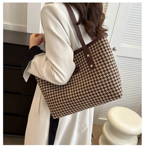 Detail of a large houndstooth tote bag with brown leather straps shown on a female model