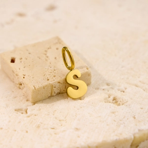 Detailed macro view of gold-plated letter S pendant on a natural stone background
