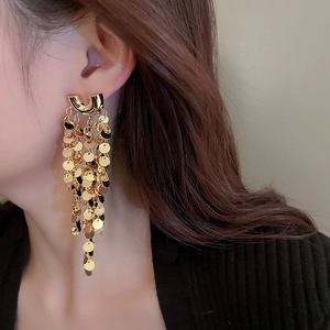 Close-up of long gold tiered sequin tassel earrings worn by a model in profile