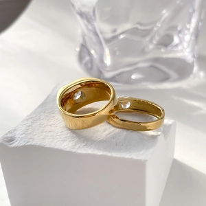 Close-up of golden couple rings with gear design and center gemstone on white stone