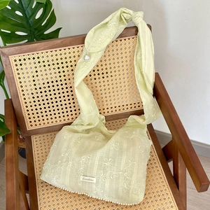 Détail du sac en mousseline avec broderie florale et perles blanches sur une chaise en bois