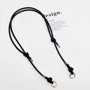 Detail of adjustable black leather bag strap featuring gold metal rings and knotted design