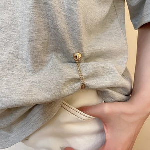 Detail view of a gold magnetic chain clip shortening the hem of a grey cotton T-shirt