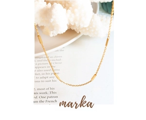 Detail showing elegant gold chain with minimalist rectangular bars on white coral background