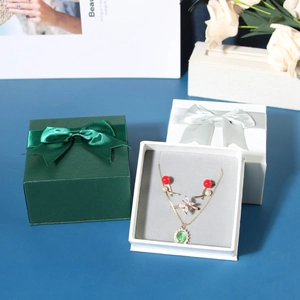 Green and white jewelry gift boxes with satin bows featuring a necklace and earrings set