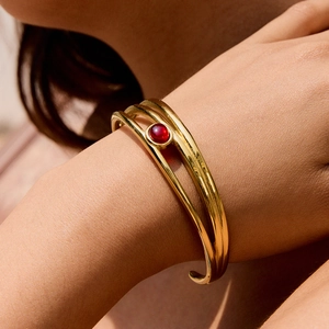 Dettaglio di un bracciale rigido in acciaio dorato a più strati con pietra naturale rossa
