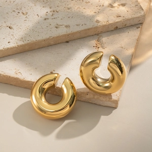 Detail of glossy 18K gold C-shaped ear cuffs displayed on decorative beige stone slabs