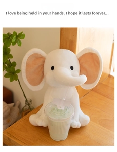 Detailed view of a soft white plush elephant toy with pink ears on a wooden surface