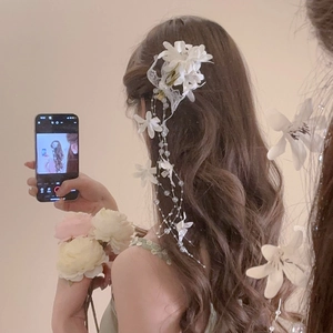 Detail of elegant white fabric flower hair clip with pearls and tassels on long wavy hair