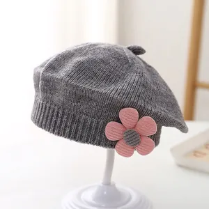 Detail of grey knitted beret featuring a soft pink flower and ribbed edge on stand
