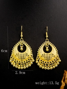 Macro shot of gold peacock earrings with bells and tassels on black background