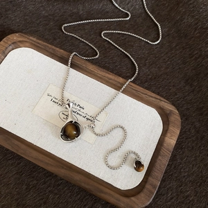 Detailed shot of tiger eye stone pendant on a silver chain over a rustic wooden tray