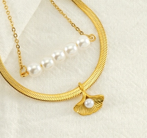 Detail of layered gold ginkgo leaf pendant and pearl choker on white fabric