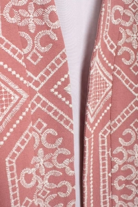 Close-up of white floral embroidery details on pink long cardigan fabric texture