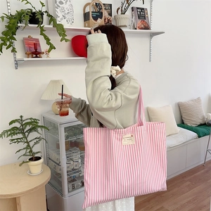 Pink and white striped canvas tote bag with a small heart label in a cozy indoor setting