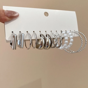 Close-up of silver geometric earring set with pearls and twisted hoops on display card