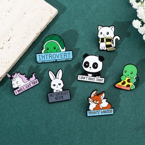 Flat lay of colorful enamel animal pins with humorous quotes on a green background