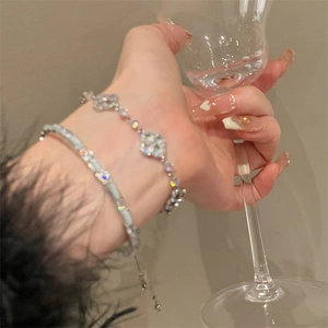 Silver flower and tennis bracelet set worn by a model holding a crystal glass