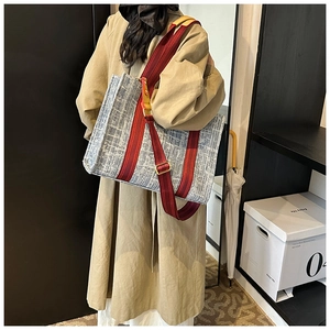 Large denim tote bag with red striped wide shoulder strap worn by model in a boutique