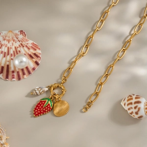Dettaglio di ciondoli a fragola e conchiglia in oro 18K con chiusura a T su sfondo spiaggia