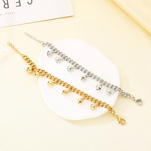 Elegant 18K gold and silver stainless steel bracelets with small bell charms on stone tray
