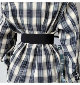 Rear view of a stylish black elastic waist belt worn over a checkered coat for women