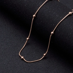 Rose gold stainless steel snake chain necklace with beads on textured black background