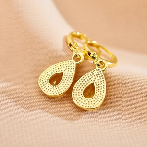 Macro detail of golden teardrop earrings with textured dots and hollow center design