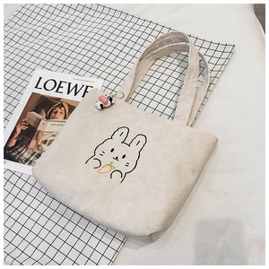 Close-up of beige corduroy tote with rabbit embroidery and a small cow plush keychain