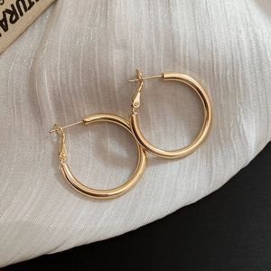 Macro shot of minimalist gold hoop earrings on soft satin fabric showcasing polished finish