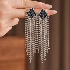 Close-up of vintage rhombic earrings featuring long sparkling tassel dangles on fingers