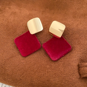 Détail de boucles d'oreilles carrées floquées rouges avec métal doré sur tissu brun