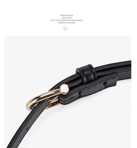 Detail of a thin black leather belt featuring a sleek golden circular metal buckle and loop