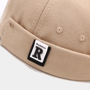 Detail of khaki docker cap featuring a textured knit fabric and stitched R letter patch