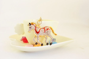 Detail of a golden horse keychain with sparkling crystals and red enamel accents