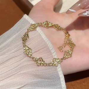 Detailed close-up of a gold hollow floral bracelet with adjustable chain on a palm background