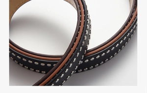 Macro shot of punk style black PU leather belt with silver rivets and brown edge detail