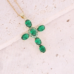 Dettaglio del ciondolo a croce in zircone verde su catena dorata su pietra