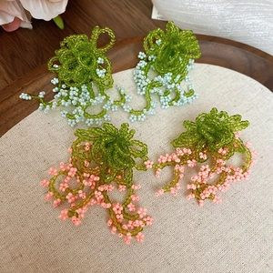 Detailed handcrafted beaded floral earrings in green pink and light blue on a wood tray
