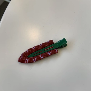 Glossy deep red wave duckbill hair clip with dark green metal base in minimalist style