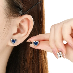 Close-up of elegant silver-tone heart studs with vibrant blue gemstones on model ear