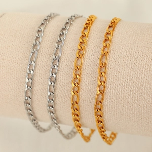 Elegant gold and silver Figaro chain bracelets displayed on a premium textured stand
